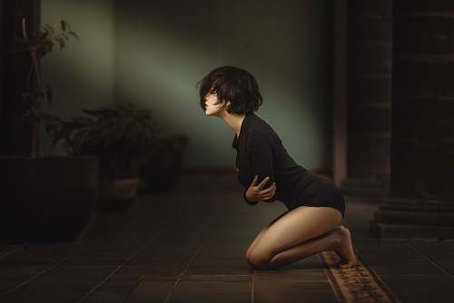 human woman kneeling with arms folded over chest inside dim-lit room person