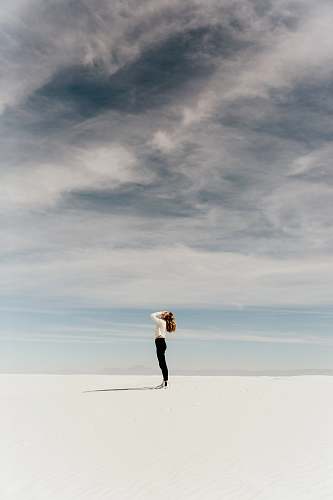 woman woman looking up to the sky while standing on white sand minimal