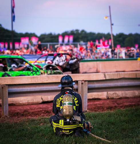 human firefighter sitting on grass near stock cars on road fireman