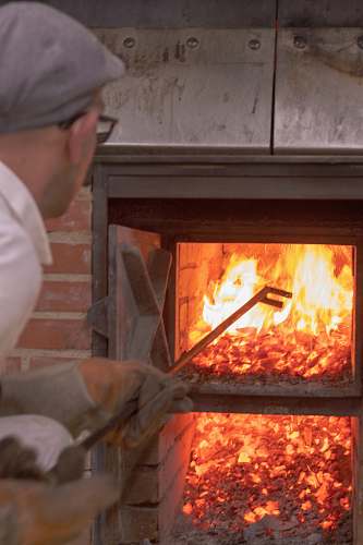 indoors man picking with long rod on wood fired oven fireplace