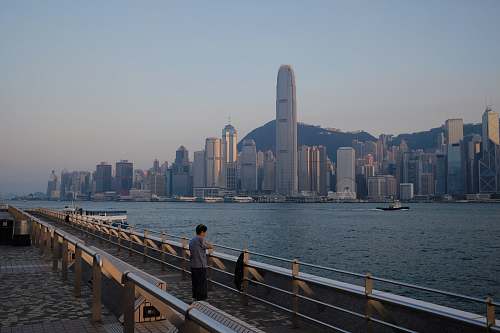 human person standing on pier near the city during day railing