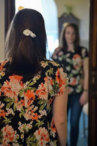 people woman wearing black and multicolored blouse and blue denim jeans facing mirror inside white concrete room human