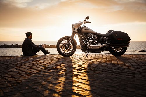 man sitting on ground beside parked silver cruiser motorcycle
