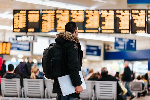 man standing inside airport looking at LED flight schedule bulletin board