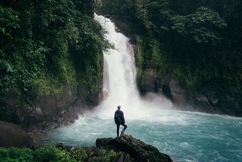 man standing on cliff near falls