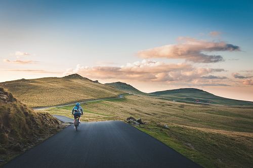 person cycling on road distance with mountain during daytime