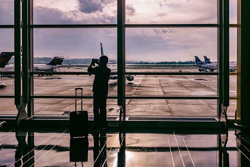 silhouette of person standing in front of glass while taking photo of plane