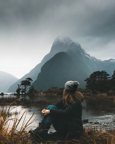 woman sitting near body of water looking at clouds