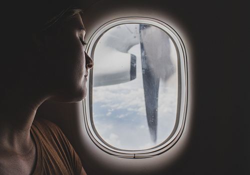 woman wearing brown scoop-neck sitting near airplane window while sleeping during flight