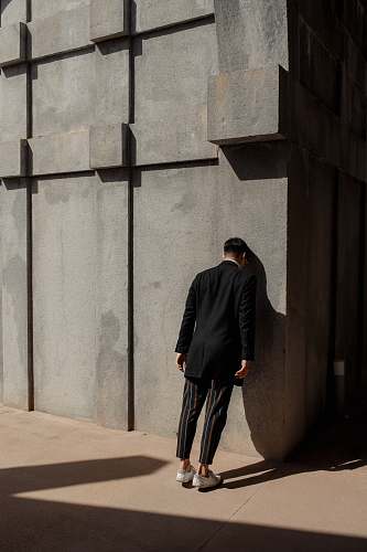apparel man in black suit banging his head on wall overcoat