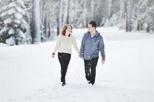 human couple walking on snow near trees during daytime person