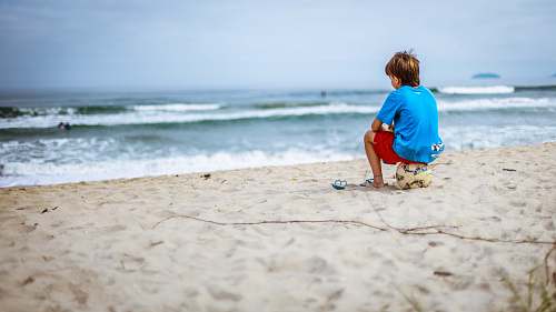 water boy sitting on ball while staring at the ocean beach