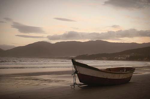 rowboat brown on seashore near body of water under cloudy sky at daytime transportation