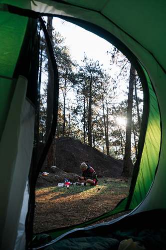 camping man sitting on grass surrounded by trees during daytime tent