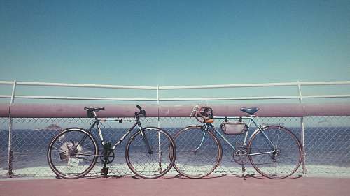 bicycle two black and gray bicycles parked near fence on seashore at daytime bike
