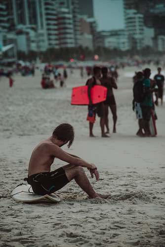 person man sitting on white surfboard on sand during daytime back