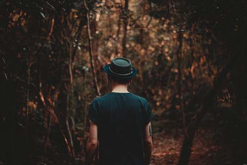 person man wearing black hat walking on forest during daytime people