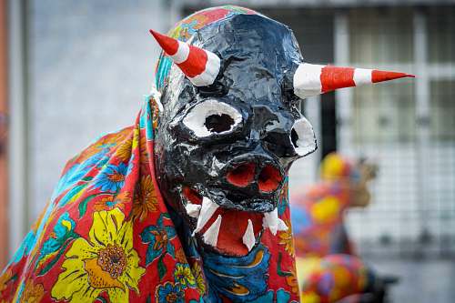 crowd person wearing monster mask covered with yellow and red floral cape festival