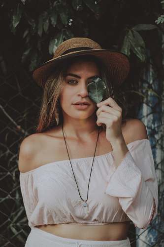 person selective focus photography of women in off-shoulder long-sleeved crop shirt holding leaf covering her one eye people