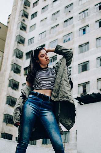 person woman wearing crop top and denim pants standing near high rise building people