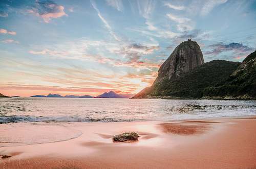 outdoors mountains near ocean under white clouds during daytime shoreline