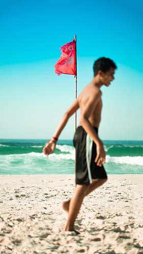 ocean selective focus photo of red flag on brown pole near body of water beach