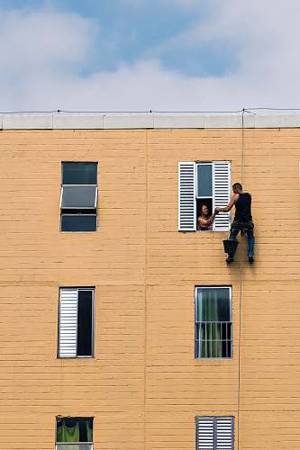 human man hanging on building near woman in window during daytime people