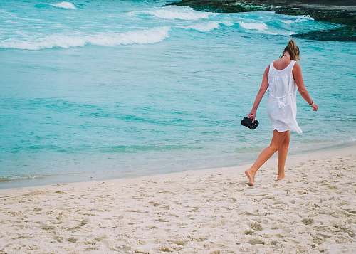 sea woman in white dress walks on white sand beach ocean