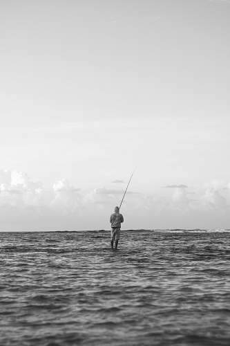 human grayscale photo of person fishing on sea outdoors