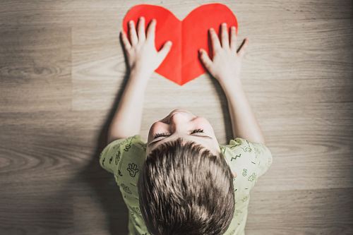 boy in green shirt holding red paper heart cutout on brown table