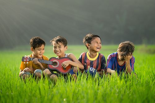 four boys laughing and sitting on grass during daytime