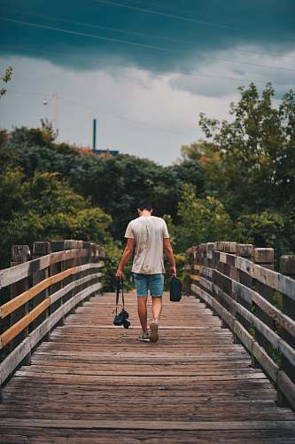 person man walking on brown wooden bridge people
