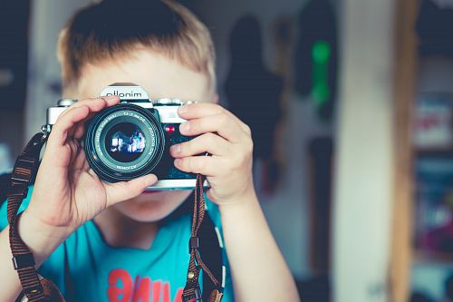 selective focus photography of boy holding gray Minolta bridge camera