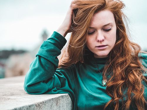 selective focus photography of woman wearing green long-sleeved top leaning on wall