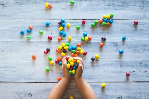 selective photo of kid holding candies on gray wooden pallet board
