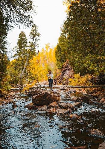 outdoors woman in white jacket standing on rock in river during daytime nature