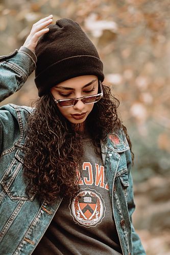 woman wearing blue denim jacket touching her hat while standing and looking down