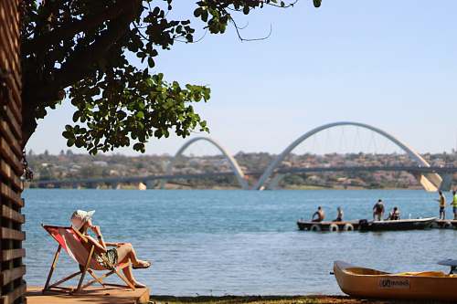 canoe person sitting on pool chair in front of sea with white suspension bridge rowboat