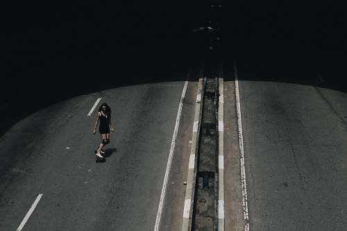 person high angle photo of woman riding on skateboard passing road grey