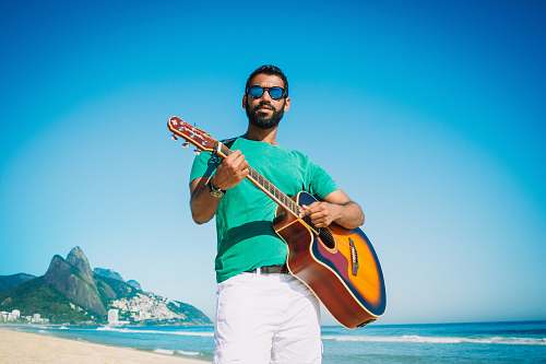 person man playing guitar near ocean during daytime people