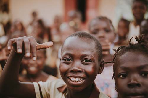 human boy in brown collared top smiling and surrounded by children face
