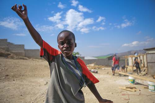 human boy wear gray and orange shirt standing while raising his left hand people