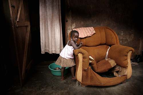 human girl standing near brown fabric sofa chair inside room people