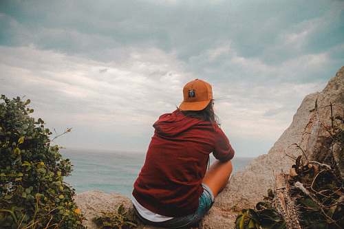 human woman sitting on beige rock under white cloudy sky at daytime people