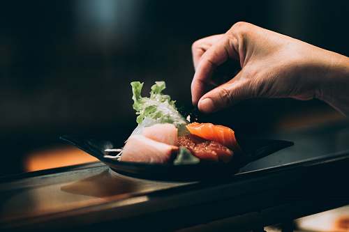 person left hand picking vegetable on plate people