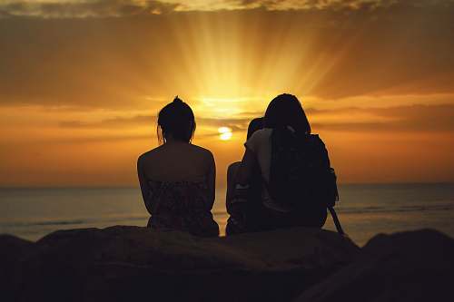 person three person sitting on brown stone while watching the sunset people