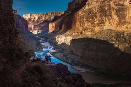 canyon two person standing on rocks facing body of water valley
