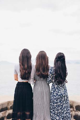 person three woman looking back and facing body of water woman