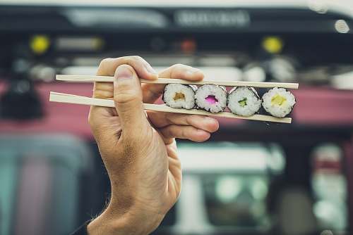human cooked sushi on chopsticks finger