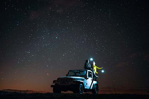 stars person sitting on top of wrangler under starry sky jeep